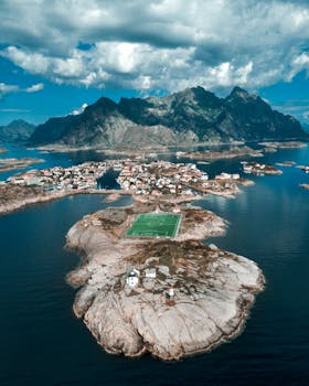 Stunning aerial view of Lofoten Islands featuring an isolated football field surrounded by azure waters and rugged mountains.