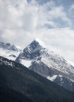Stunning view of a snow-capped mountain peak in Tux, Tirol, Austria under a cloudy blue sky.