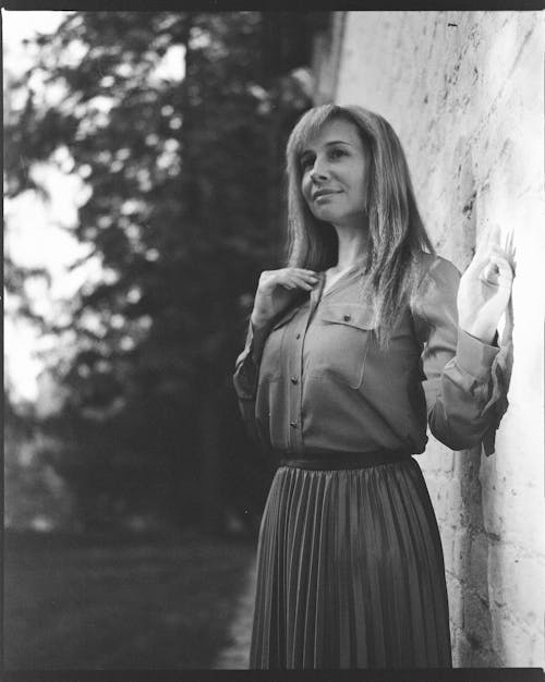 Black and White Photo of a Woman Standing by the Wall 