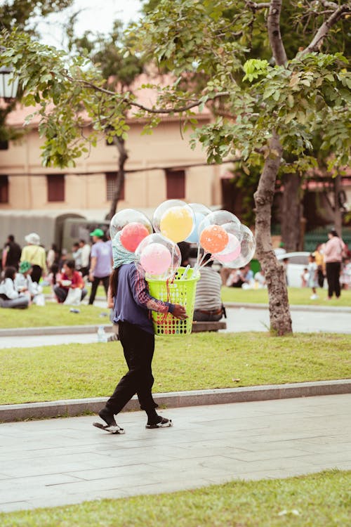 Woman Walking in a Green Park with Multicoloured Balloons