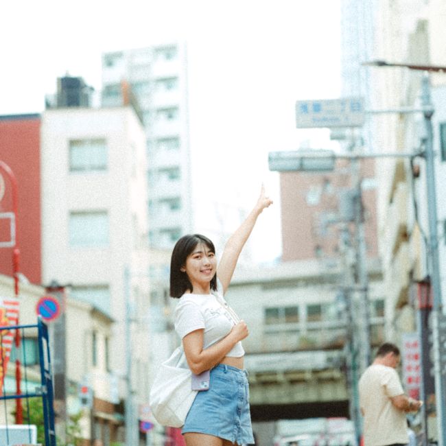 Asian woman in a bustling city street, pointing upwards with a smile.