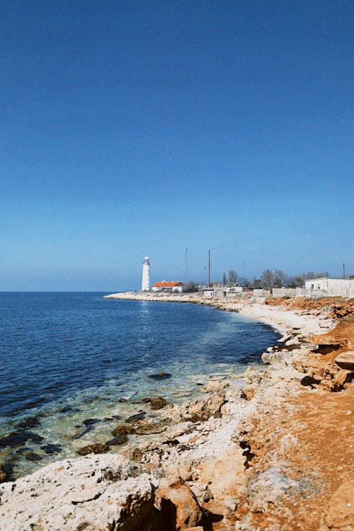 View of a Coast and Lighthouse under Clear Blue Sky 