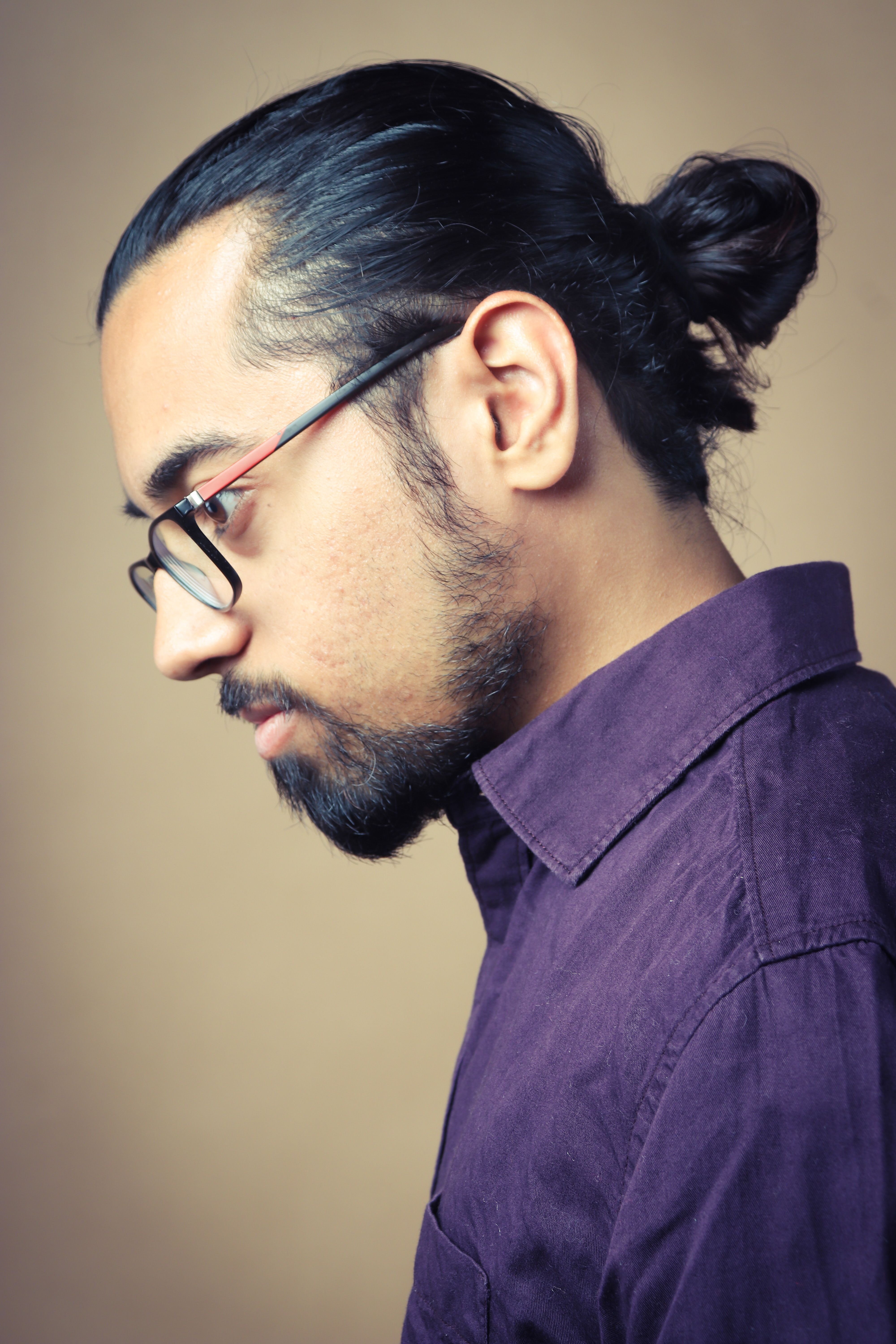 Thoughtful side profile portrait of a young man with glasses wearing a purple shirt.