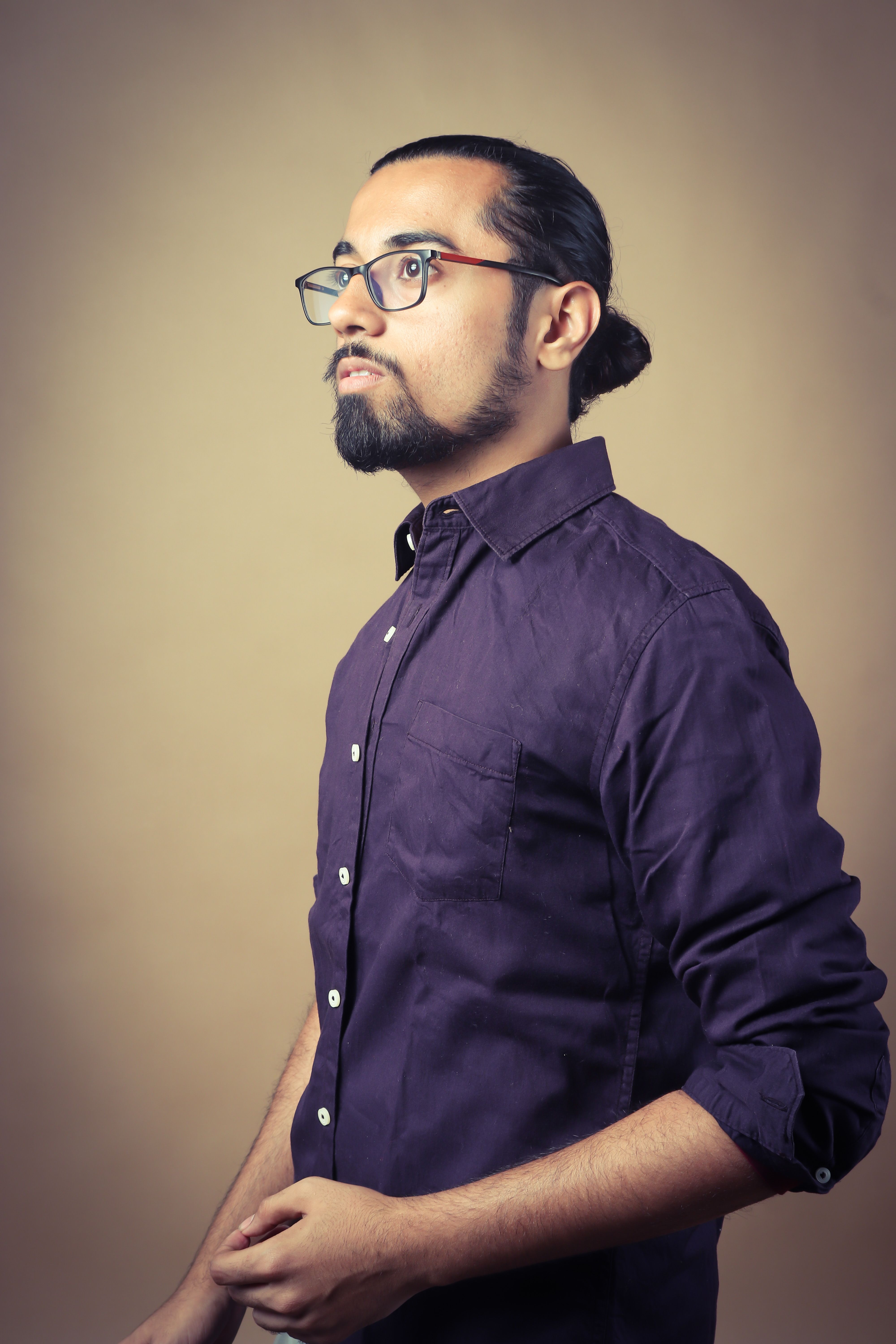 Portrait of a young man with beard and eyeglasses in a purple shirt against a yellow background.