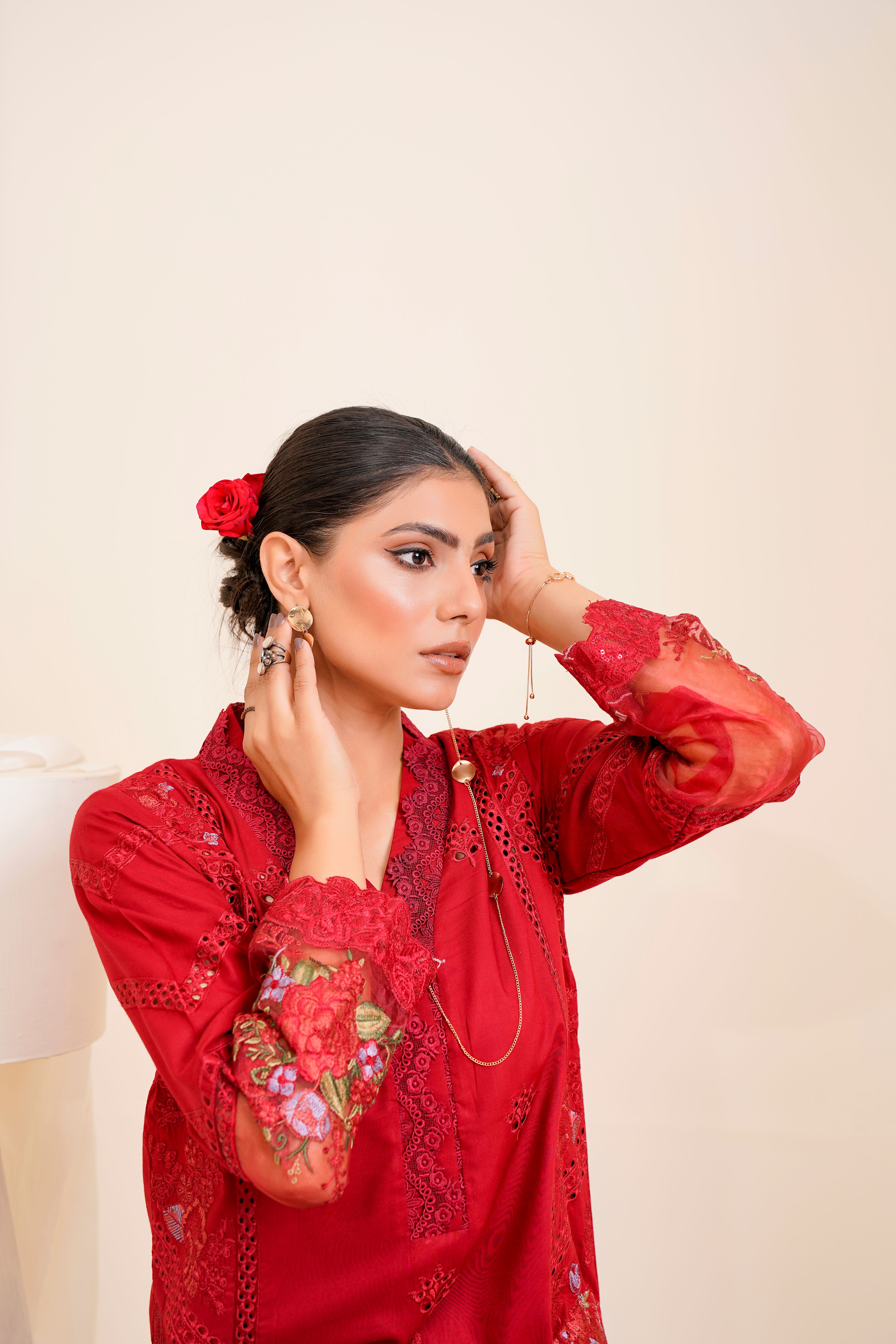 A young woman posing in a studio wearing a stylish red blouse with embroidery.