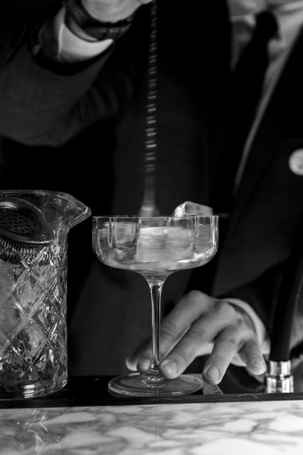 A stylish bartender in a suit artfully stirring a cocktail at a bar counter.