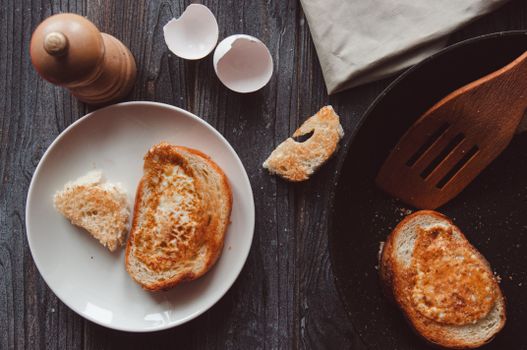 Rustic breakfast setup with toast, eggshells, and wooden utensils on a dark wooden table.