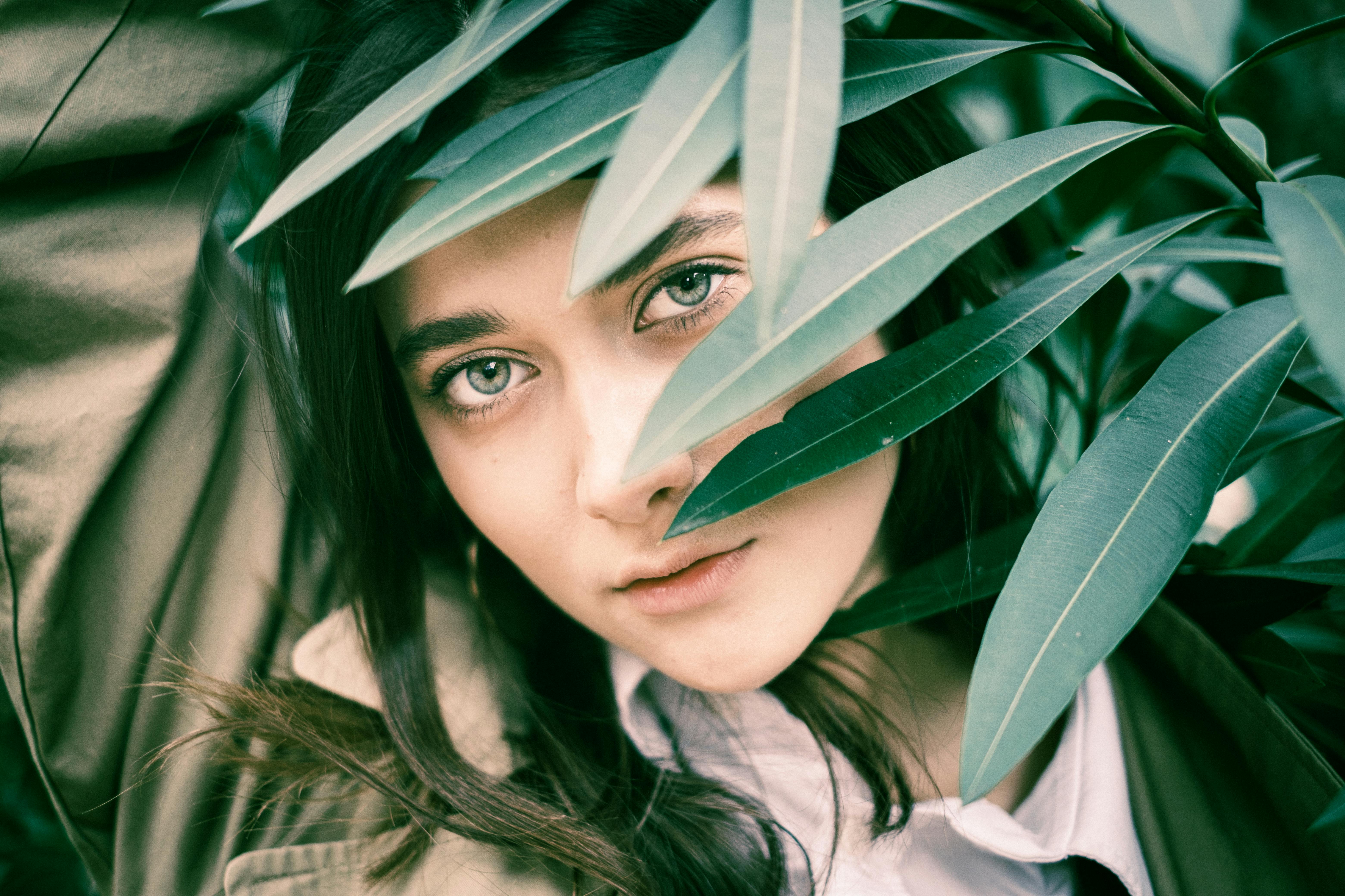 A woman’s face framed by green leaves, depicting natural beauty and mystery.