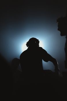 Backlit silhouette of a DJ mixing music in an atmospheric nightclub setting.