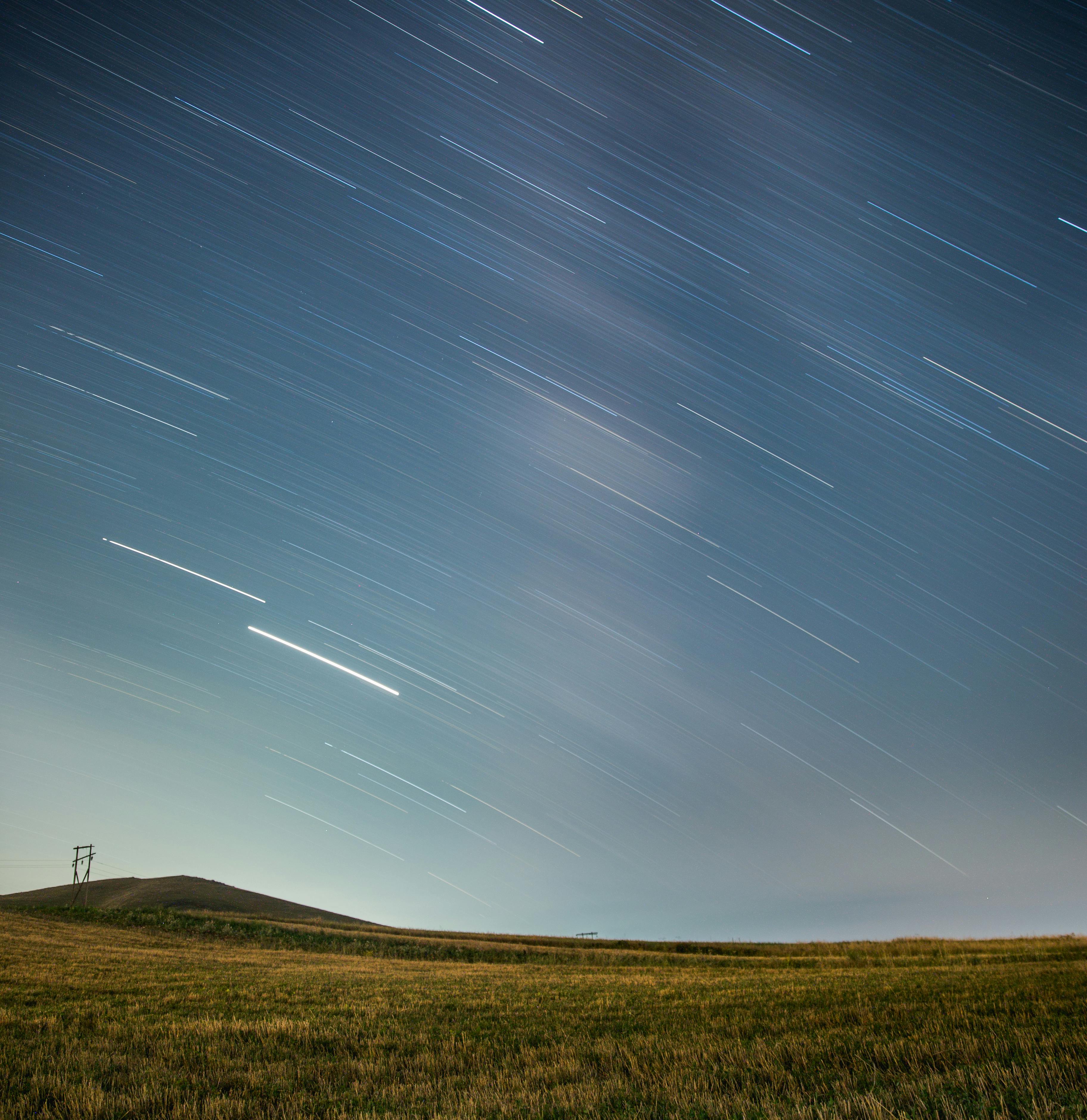 A stunning display of star trails across a night sky over open fields, showcasing the Earth's rotation.