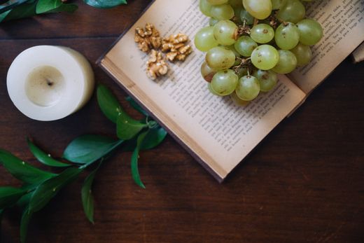 Still life of grapes, walnuts and a candle on an open book — Douglas Mendes on Pexels