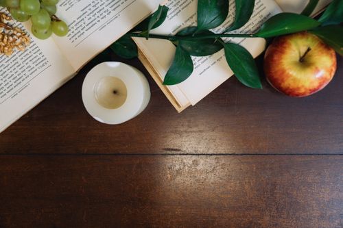 Free A tranquil still life featuring an open book, apple, candle, and green leaves on a wooden table. Stock Photo