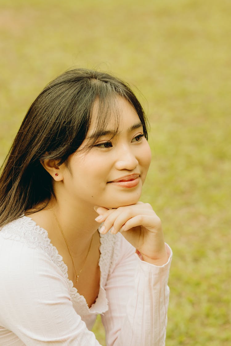 Young Woman Sitting Outside With Hand Under Her Chin 