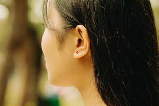 Profile view of a woman with long dark hair wearing an earring, captured in an outdoor park setting.
