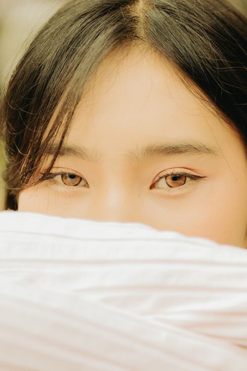 Free Close-up portrait of a young Asian woman covering her face, focusing on expressive eyes. Stock Photo