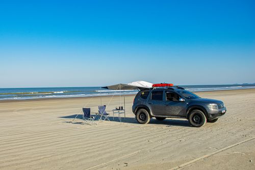 Free A car parked on Ilha Comprida beach with camping gear under a clear blue sky. Stock Photo