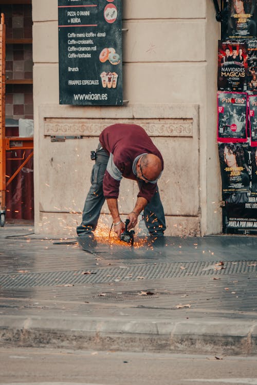 Man Cutting Metal Grating with Angle Grinder on the Sidewalk