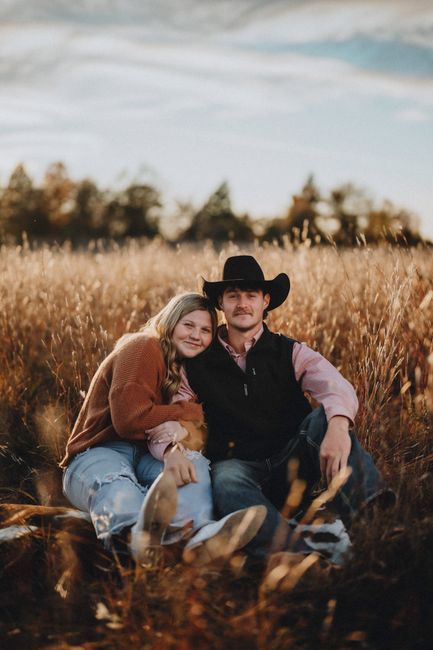 A couple in a cowboy hat and casual attire embrace in a sunlit meadow, exuding warmth and love.