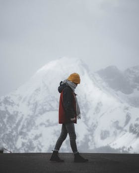 Person in warm clothing walking in snowy mountain landscape, ideal for winter travel themes.