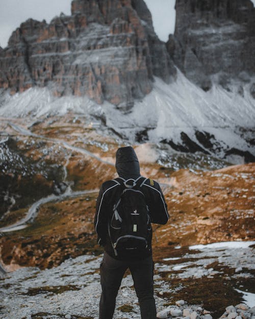 Back View of a Man with a Backpack Standing on a Field in Mountains