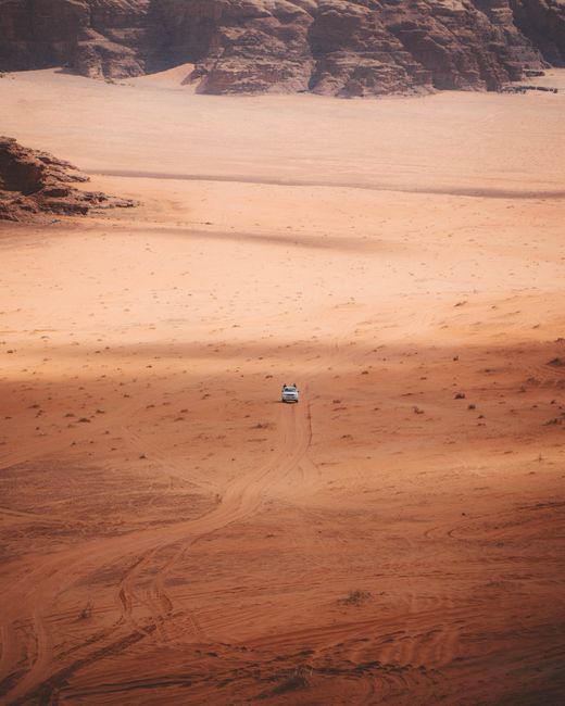 Aerial view of a lone car on a dirt road in the expansive Wadi Rum desert, Jordan.