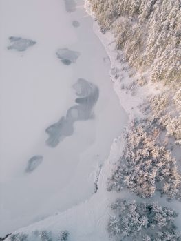 Aerial view of a snow-covered forest and frozen lake in Ogre, Latvia during winter.