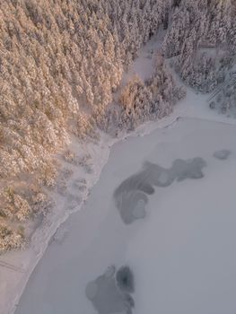 Breathtaking aerial view of a frozen lake surrounded by snow-covered trees in Ogre Municipality, Latvia.