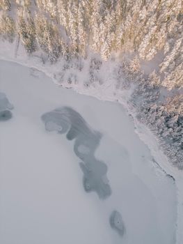 Scenic aerial shot of a frozen lake bordered by snow-covered forest in winter.