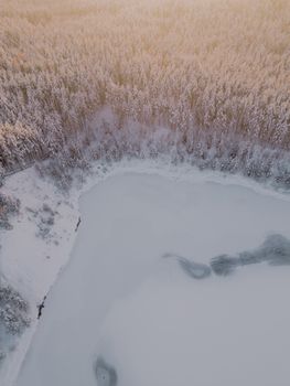 A stunning aerial shot of a frozen lake surrounded by dense snowy forest in winter.