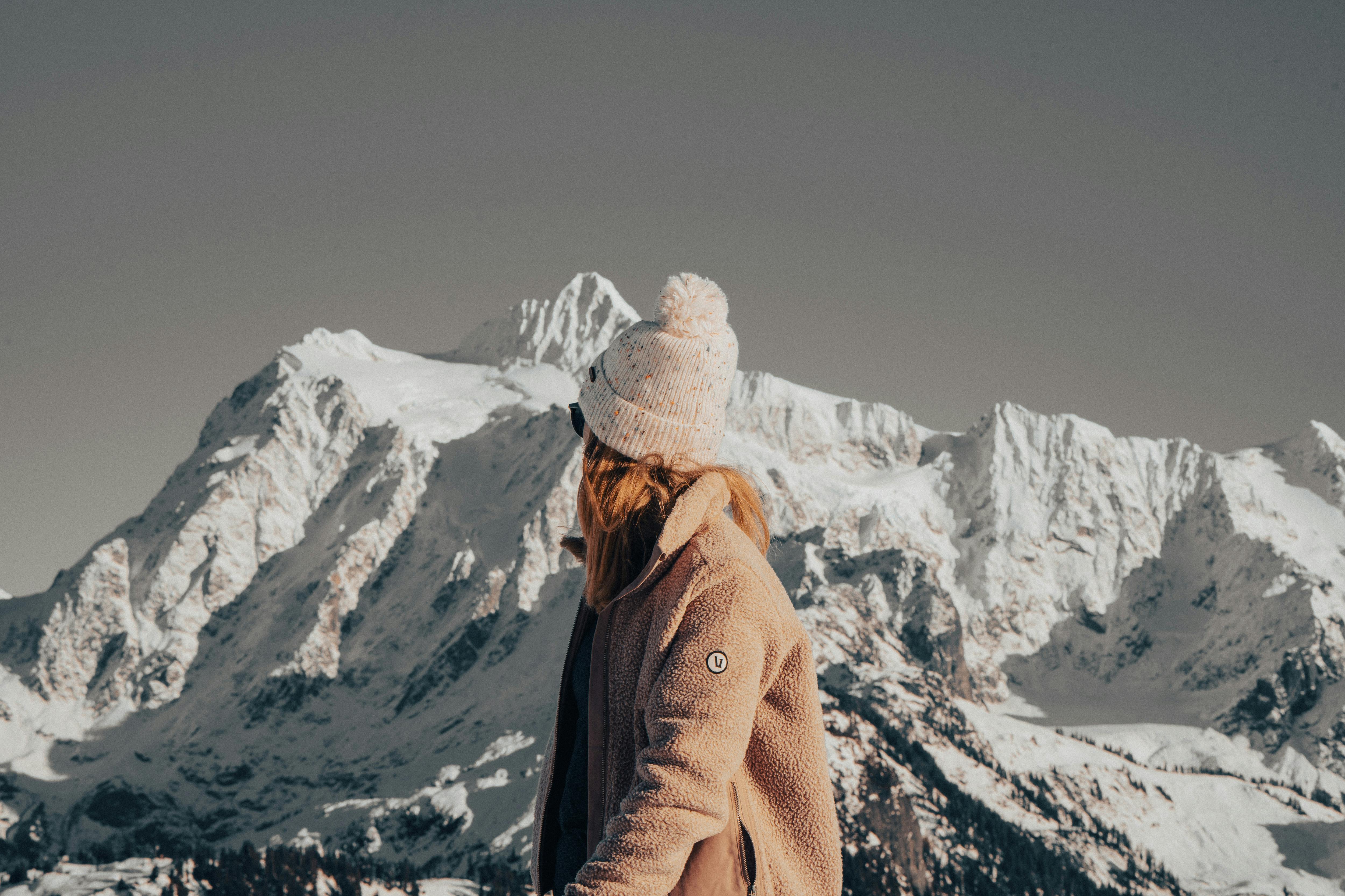 Prescription Goggle Inserts - A woman in winter attire gazes thoughtfully at a majestic snowcapped mountain range.