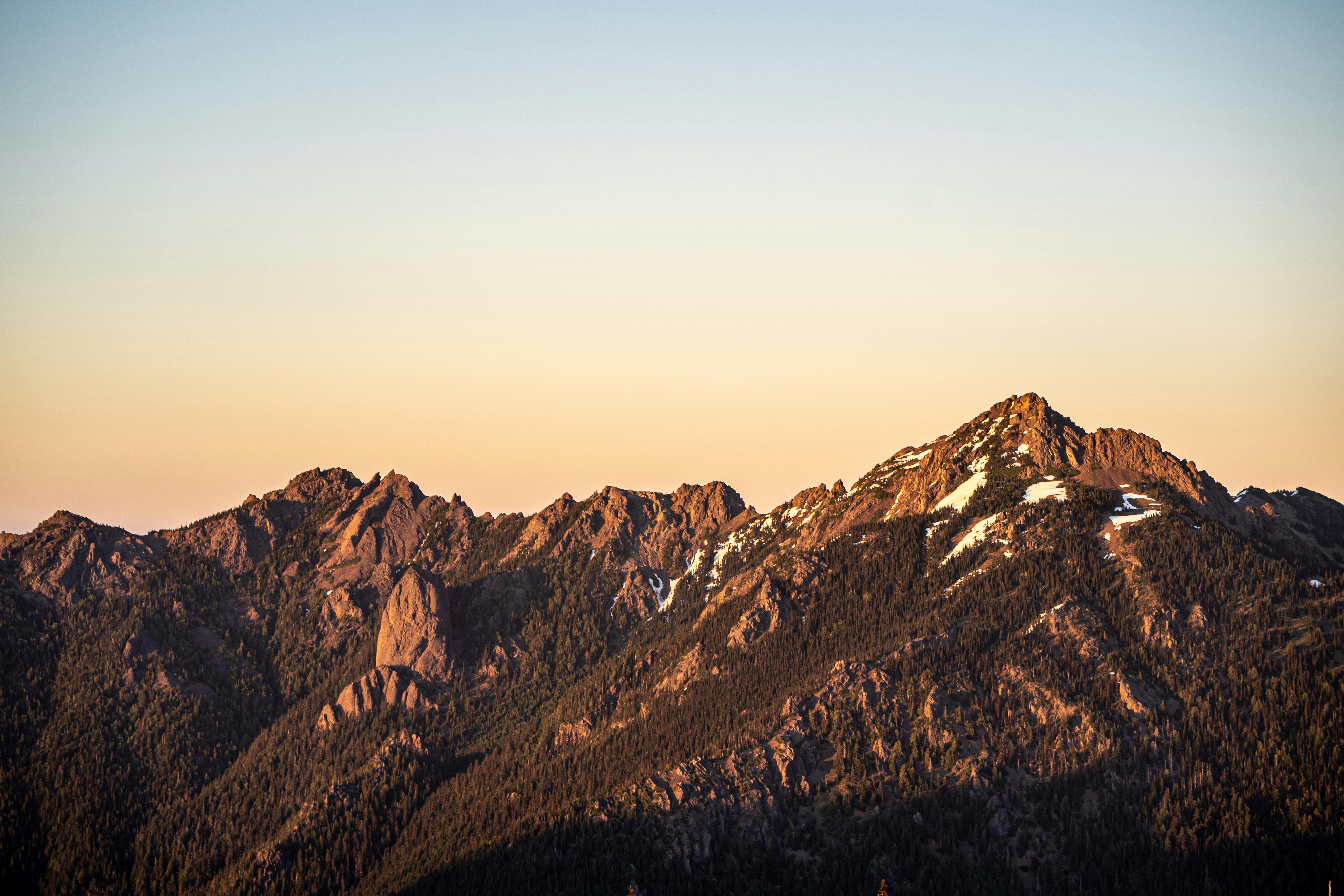 Stunning view of the Olympic Mountains at sunrise, showcasing rocky peaks and snow patches.