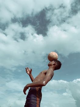 Teenager skillfully balances a soccer ball outdoors under a dramatic cloudy sky in India.