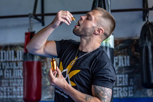 A muscular man in a gym takes a liquid supplement with a dropper.