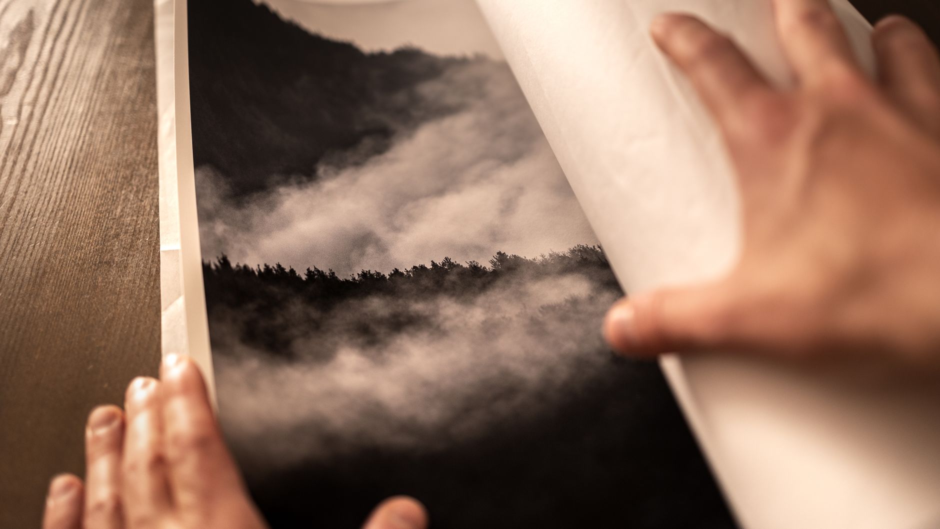 Hands unwrapping a black and white forest photograph for display.