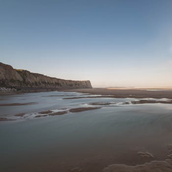 Serene view of a coastal cliff and beach during low tide, capturing the tranquil mood and natural beauty.