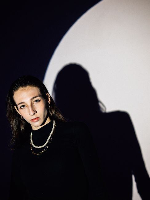 Portrait of a woman in a black sweater with striking shadow play in a studio setting.