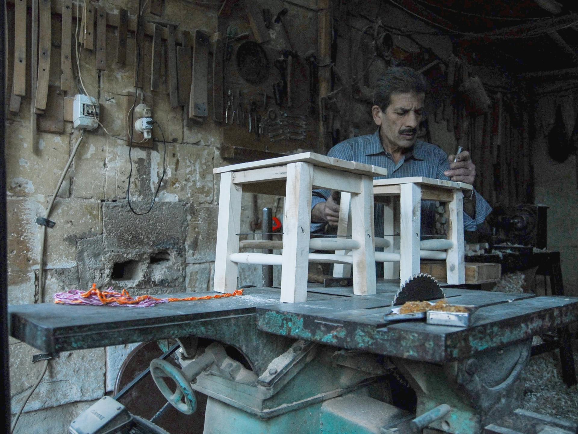 A dedicated carpenter at work crafting wooden stools in a rustic workshop setting.