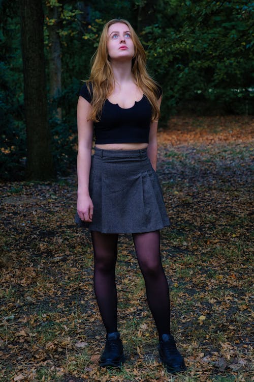 Young Woman in a Skirt Standing in a Park and Looking Up 