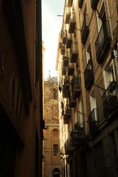 Charming view of a sunlit alley flanked by historic stone buildings in Barcelona, Spain.