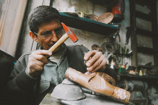An artisan skillfully uses a hammer in a rustic workshop, showcasing traditional craftsmanship.