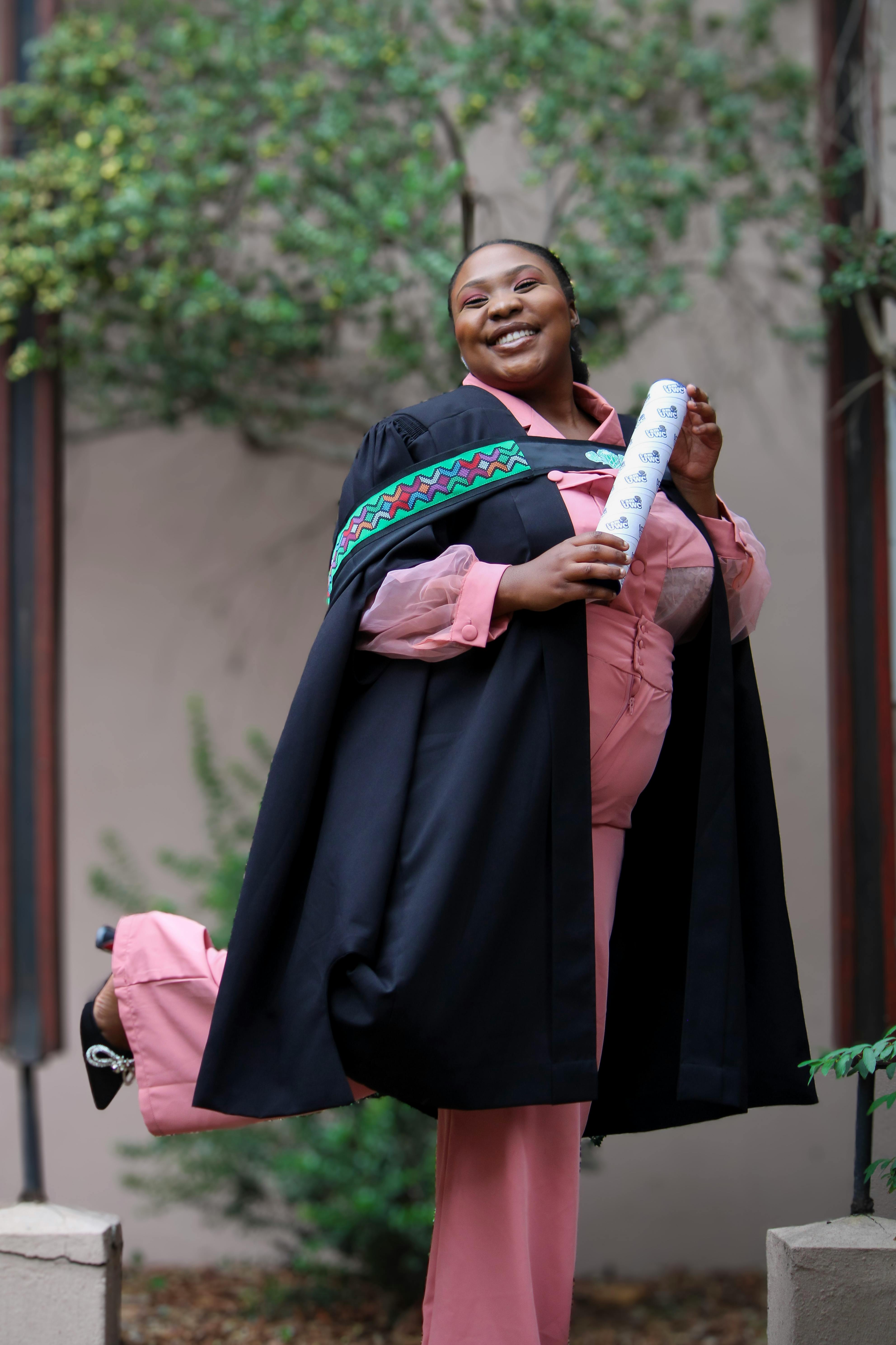 A woman in a pink gown and cap holding a diploma · Free Stock Photo