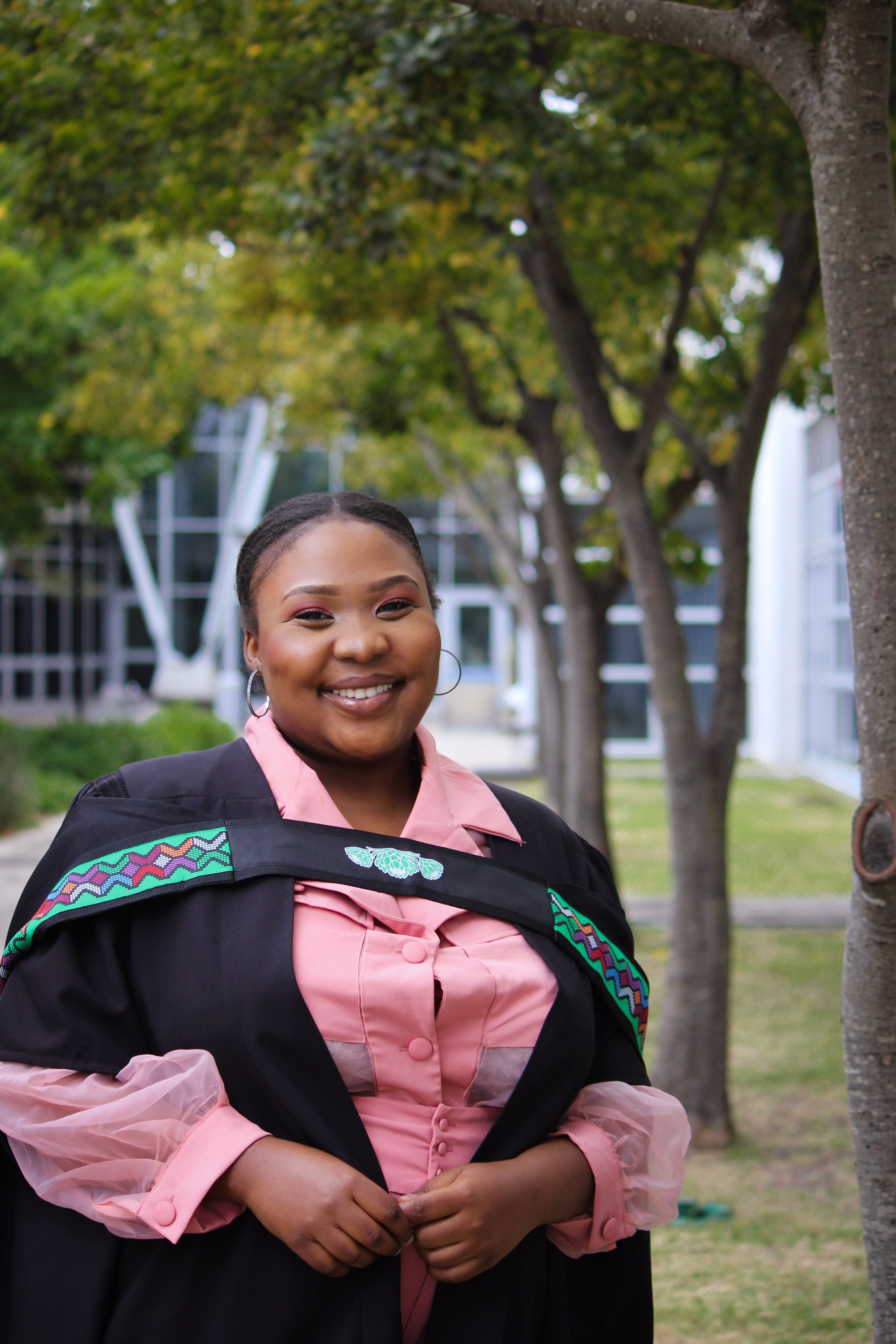 A joyful young woman in graduation attire smiling outdoors against a modern building background.