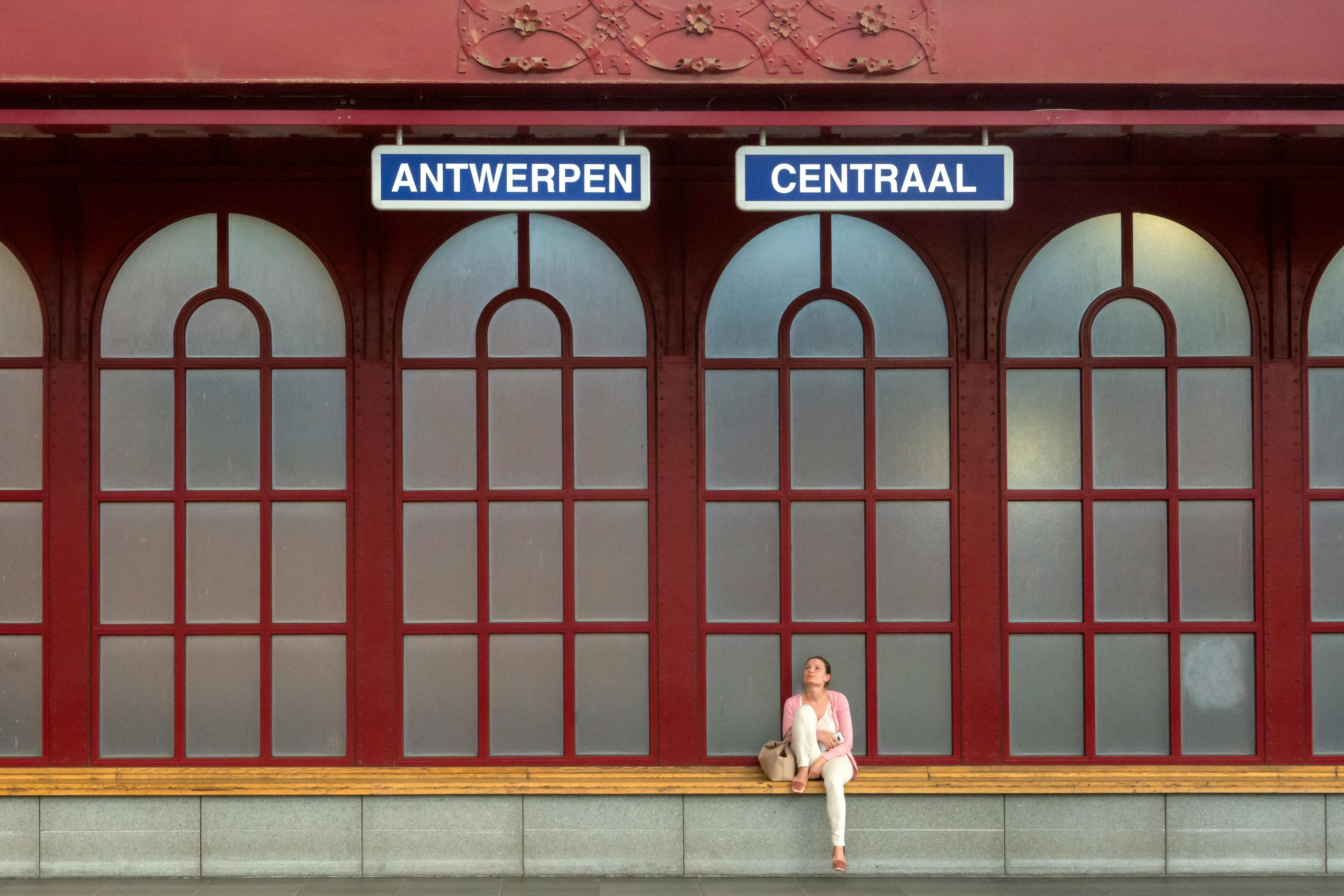 A woman seated at Antwerp Central Station's platform under decorative arches.