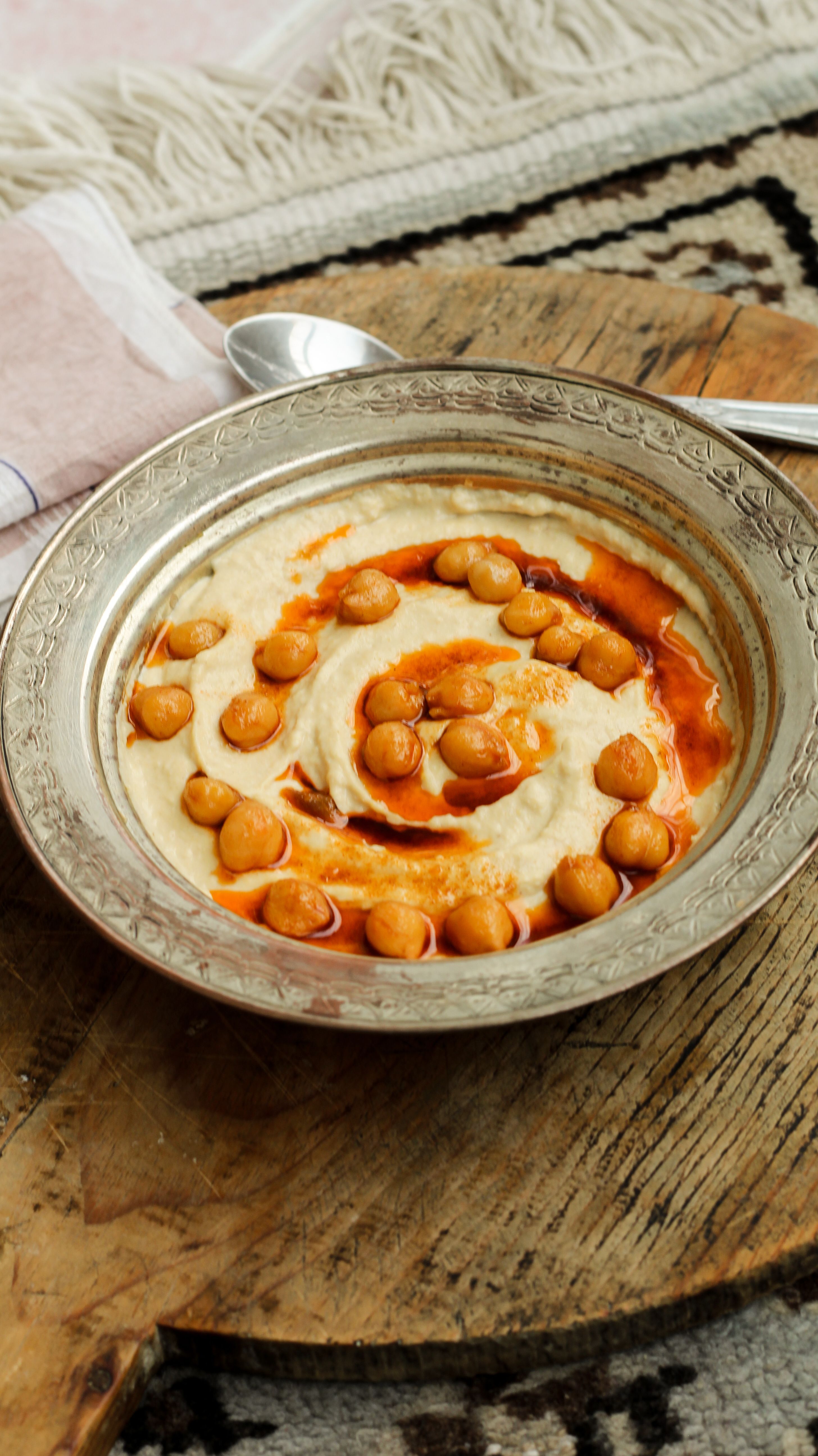 Top-down view of creamy hummus topped with chickpeas and spicy garnish on a rustic wooden board.