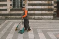 Elderly man sweeping courtyard in an urban setting with classic architecture.