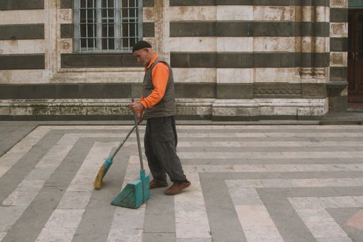 Elderly man sweeping courtyard in an urban setting with classic architecture.