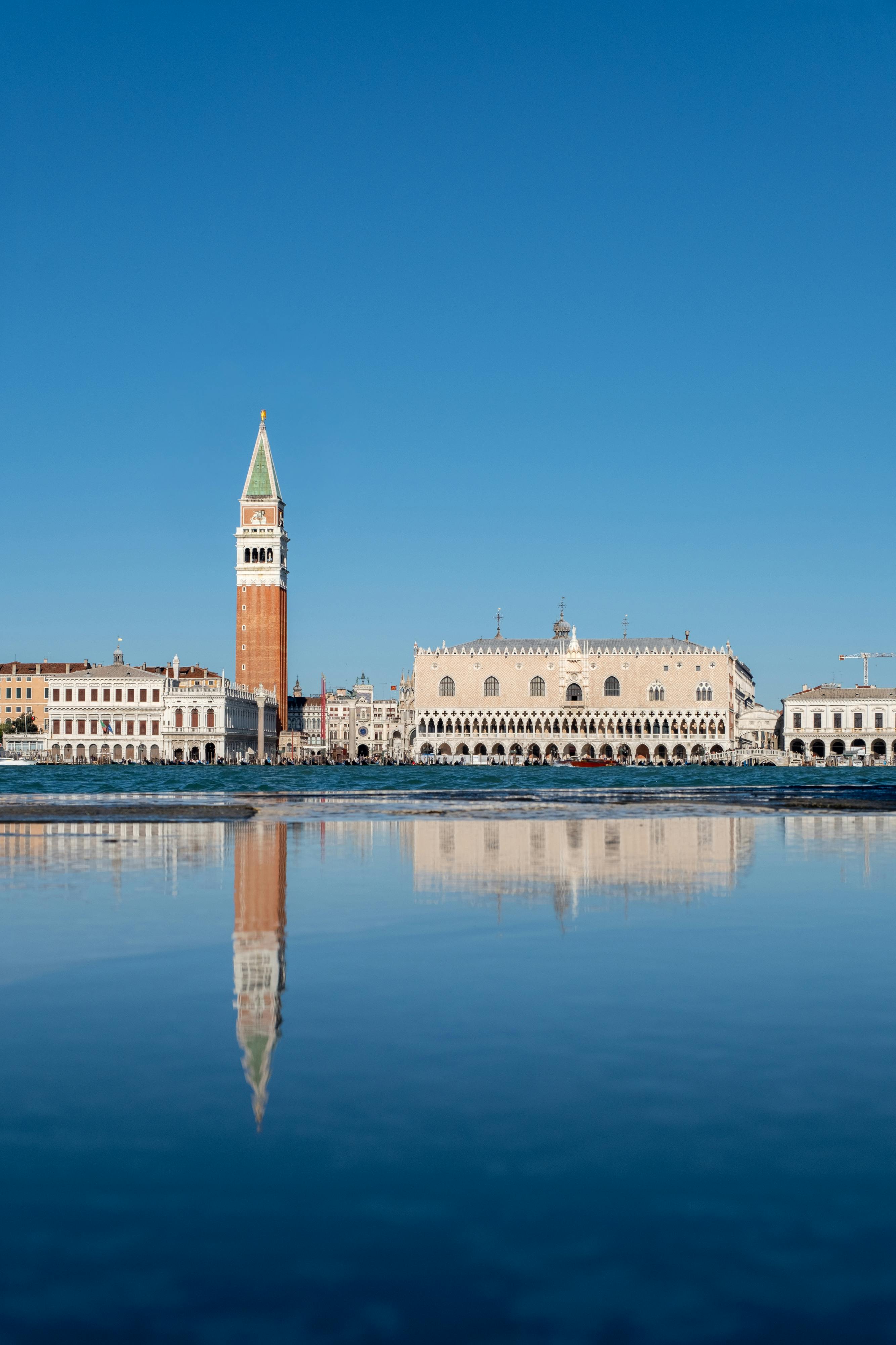 Stunning reflection of Doge's Palace and St Mark's Campanile in Venice under a clear blue sky.