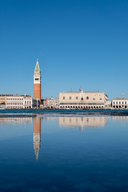 Stunning reflection of Doge's Palace and St Mark's Campanile in Venice under a clear blue sky.