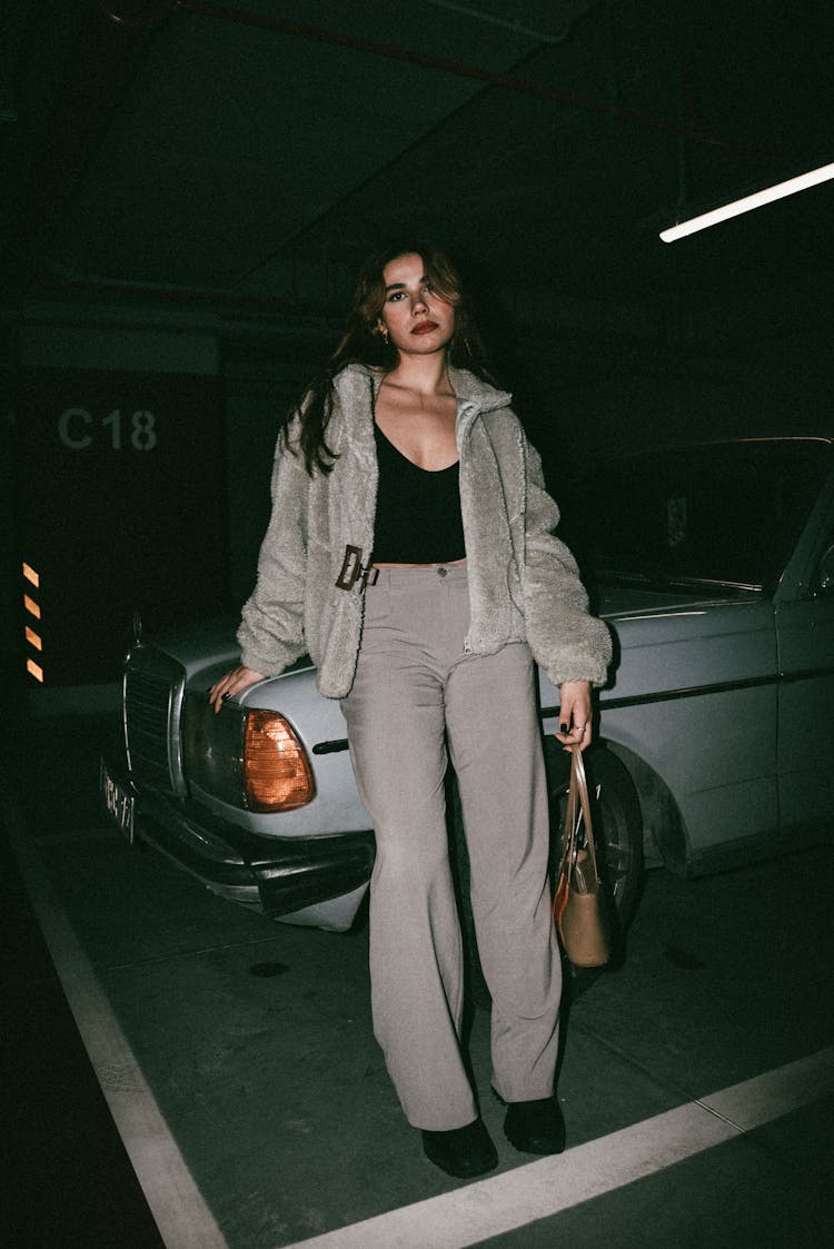 Woman In Jacket And With Bag In Parking Lot