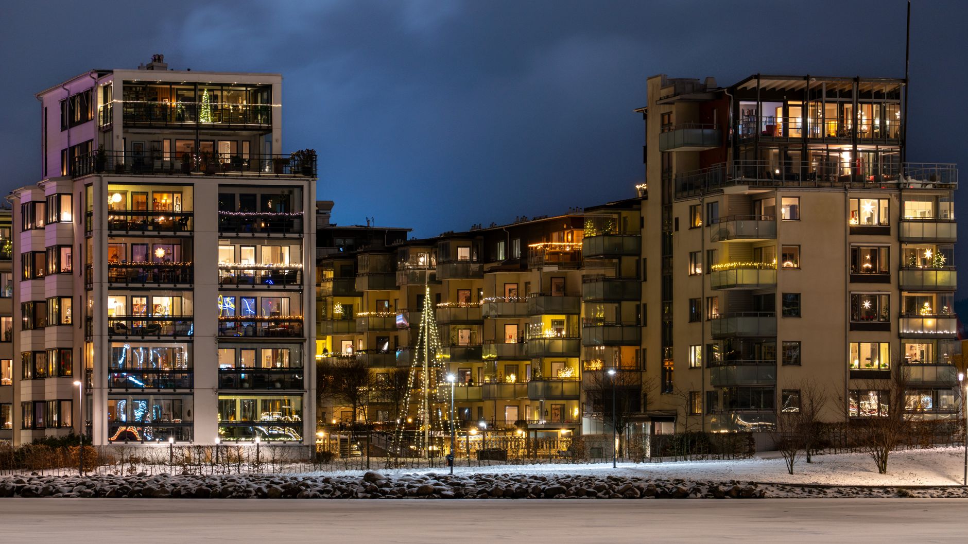 Illuminated apartment buildings at night with festive decorations in a snowy setting.
